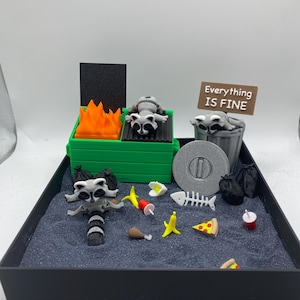 May include: A miniature diorama featuring a raccoon-themed scene. A green trash can with orange flames and a raccoon figurine. A sign reads "Everything IS FINE". Other elements include a trash can, food items, and black trash bags.