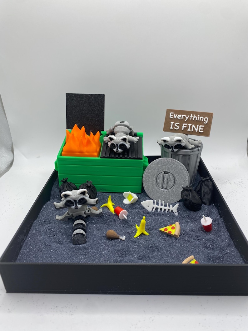 May include: A miniature diorama featuring a raccoon-themed scene. A green trash can with orange flames and a raccoon figurine. A sign reads "Everything IS FINE". Other elements include a trash can, food items, and black trash bags.