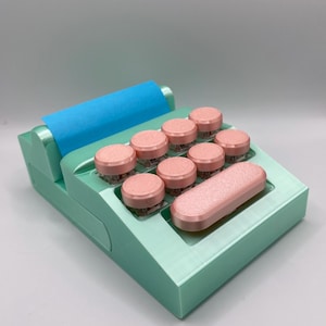 Könnte beinhalten: Eine mintgrüne und rosa mechanische Tastatur mit einer blauen Walze. Die Tastatur hat runde, rosa Tastenkappen und eine lange, rosa Leertaste. Das Design ist modern und farbenfroh.