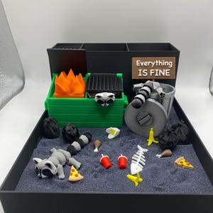 May include: A miniature diorama featuring a green dumpster with orange flames, a raccoon, trash, and the text "Everything IS FINE." The scene includes a trash can, pizza slices, and other food items.