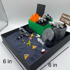 May include: A miniature diorama scene in a 6-inch square black tray. The scene includes a green grill with orange flames, raccoons, a trash can, and scattered food items. A sign reads "Everything is Fine."