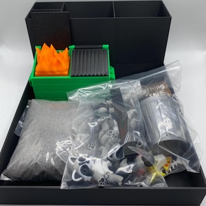May include: A black box containing miniature items. Includes a green dumpster with orange flames, a bag of gray sand, and bags of small raccoon figures. Also includes a miniature trash can and pizza slices.