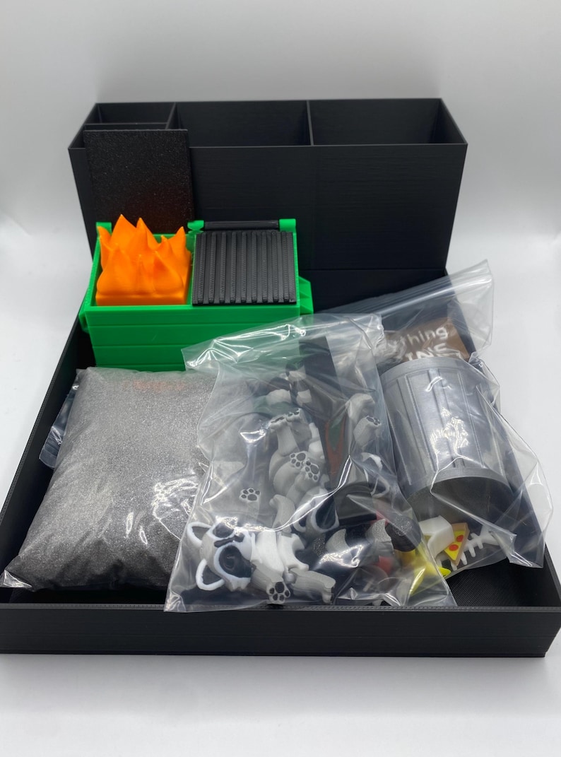 May include: A black box containing miniature items. Includes a green dumpster with orange flames, a bag of gray sand, and bags of small raccoon figures. Also includes a miniature trash can and pizza slices.