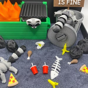 May include: A miniature diorama featuring a green dumpster with a raccoon head, a trash can with a raccoon, and various food items. A sign reads "Everything IS FINE". Includes pizza, fish bones, and soda cups.