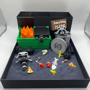 May include: A miniature diorama featuring a raccoon-themed scene. The scene includes a green dumpster with a fire, a trash can, and various food items like pizza and chicken. A sign reads "Everything is Fine."