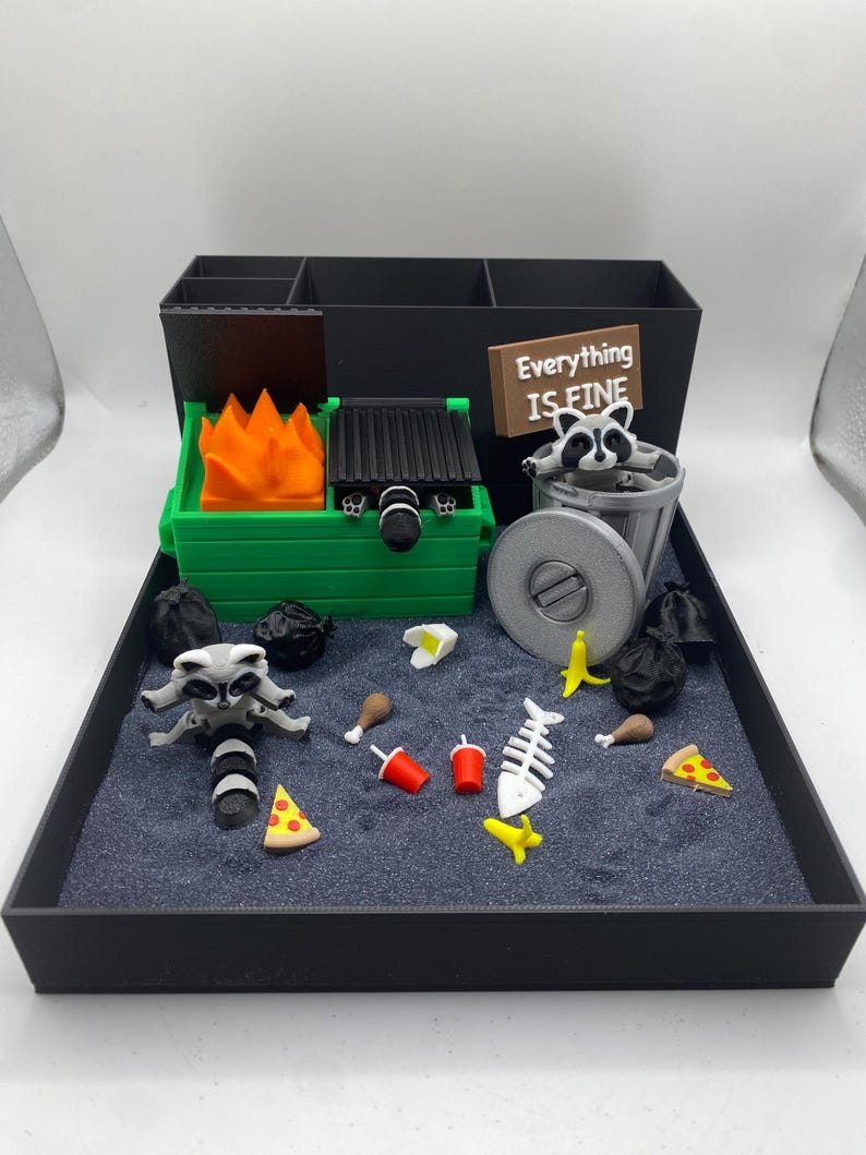 May include: A miniature diorama featuring a raccoon-themed scene. The scene includes a green dumpster with a fire, a trash can, and various food items like pizza and chicken. A sign reads "Everything is Fine."