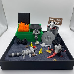 May include: A miniature diorama featuring a green dumpster with orange flames, a raccoon, and several opossums. The scene includes trash, a pizza slice, and a sign that reads "Everything is Fine."