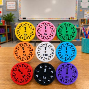 May include: A set of nine circular math multiplication tools in yellow, pink, green, orange, white, blue, red, black, and purple. Each tool features a central gear with an arrow, a multiplication factor, and a ring of numbers from 1 to 10.