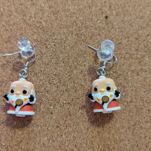 May include: A pair of silver earrings with a cartoon character charm. The charm is a white figure with a red and orange outfit and a white beard.