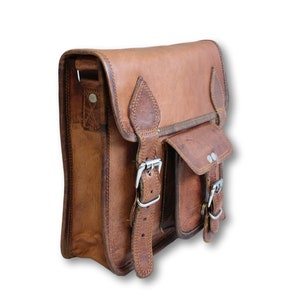 May include: A brown leather messenger bag with two buckles and a flap pocket. The bag has a strap and a small pocket on the front.