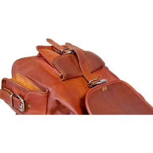 May include: A brown leather backpack with multiple compartments and silver buckles. The bag has a rectangular shape with a flap closure and adjustable straps. The leather has a natural, textured appearance.