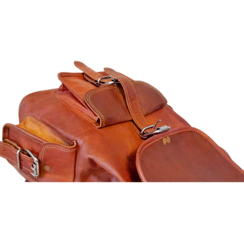May include: A brown leather backpack with multiple compartments and silver buckles. The bag has a rectangular shape with a flap closure and adjustable straps. The leather has a natural, textured appearance.