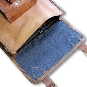 May include: Open brown leather messenger bag with a blue fabric lining. The bag has a zipped closure and a flap with a buckle.