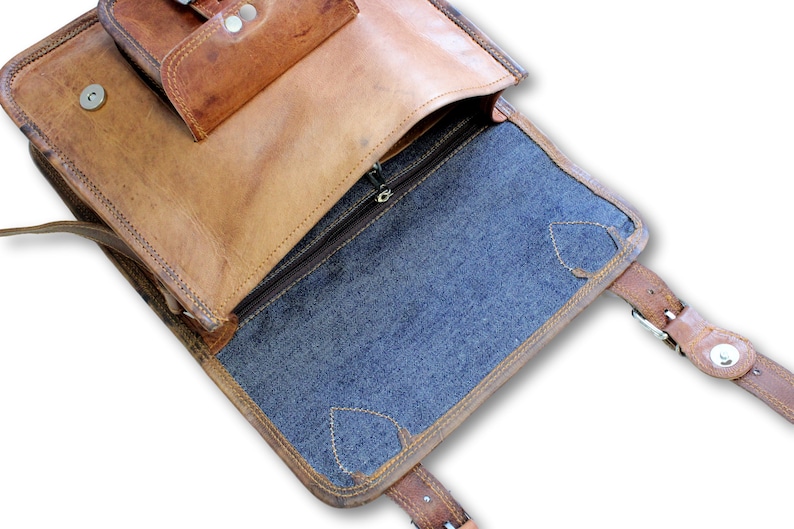 May include: Open brown leather messenger bag with a blue fabric lining. The bag has a zipped closure and a flap with a buckle.