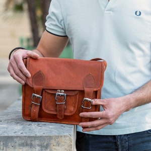 May include: A brown leather satchel bag with multiple buckles and a flap closure. The bag has a front pocket and a strap for carrying over the shoulder.
