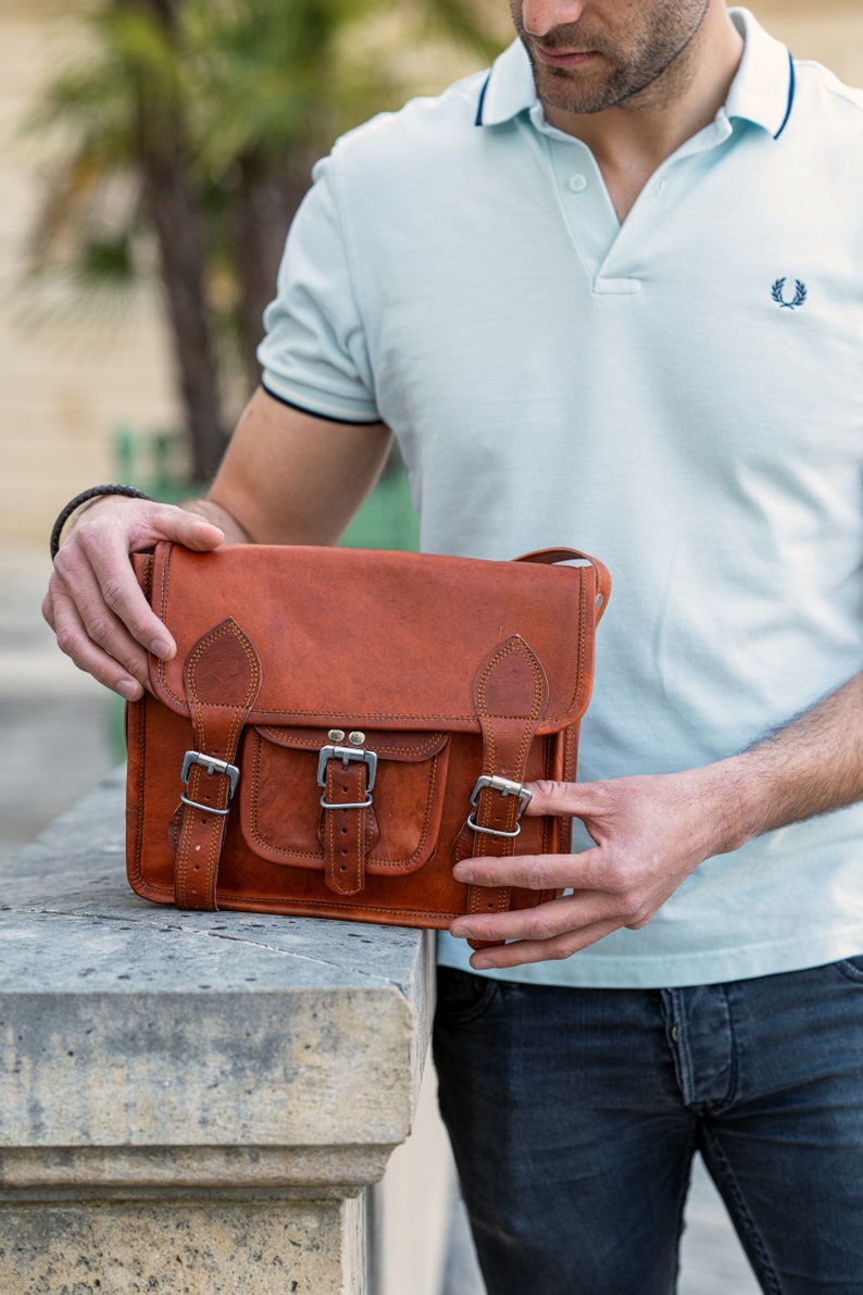 May include: A brown leather satchel bag with multiple buckles and a flap closure. The bag has a front pocket and a strap for carrying over the shoulder.