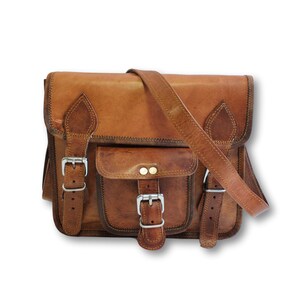 May include: A brown leather satchel bag with two front pockets and a buckle closure. The bag has a long adjustable strap.