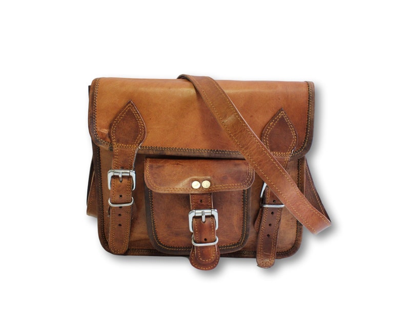 May include: A brown leather satchel bag with two front pockets and a buckle closure. The bag has a long adjustable strap.