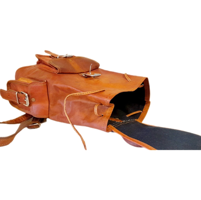 May include: A brown leather backpack with multiple compartments and adjustable straps. The bag features a flap closure with a metal buckle and a drawstring opening. The backpack has a vintage, rustic appearance.