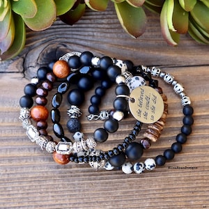 Peut inclure: Un ensemble de six bracelets en perles noires, brunes et blanches. Les bracelets sont empilés sur une surface en bois. L'un des bracelets a un charme argenté avec le texte "She believed she could... so she did."