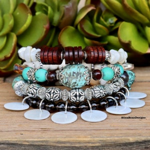 May include: A set of five bracelets featuring a mix of materials, including wood, turquoise, silver, and white shell. The bracelets are stacked on a wooden surface.