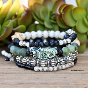 May include: A set of six bracelets featuring black, white, and green beads. The bracelets are stacked on top of each other and include a large green and white patterned bead.