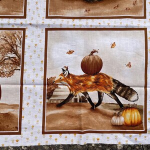 K&ouml;nnte beinhalten: Stoffpaneel mit einem Fuchs, der einen K&uuml;rbis tr&auml;gt, umgeben von K&uuml;rbissen und Herbstbl&auml;ttern. Das Design ist mit einem braunen Rahmen und einem wei&szlig;en Hintergrund mit kleinen gelben Blumenmustern versehen. Die Kanten haben eine gewellte Bord&uuml;re.