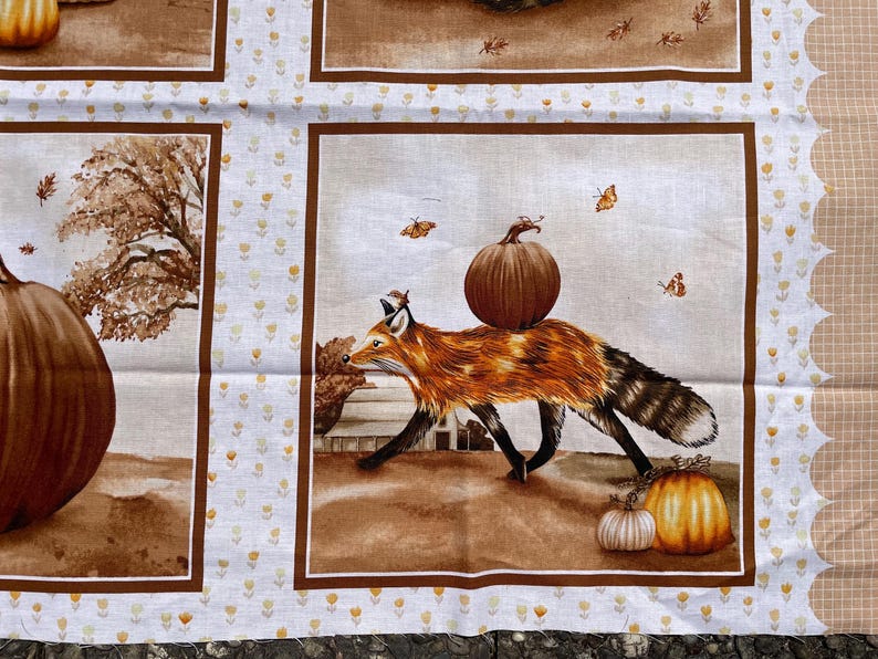 K&ouml;nnte beinhalten: Stoffpaneel mit einem Fuchs, der einen K&uuml;rbis tr&auml;gt, umgeben von K&uuml;rbissen und Herbstbl&auml;ttern. Das Design ist mit einem braunen Rahmen und einem wei&szlig;en Hintergrund mit kleinen gelben Blumenmustern versehen. Die Kanten haben eine gewellte Bord&uuml;re.