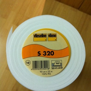 Op de afbeelding: Een rol witte verstevigingsstof met een geel en oranje etiket. Het etiket luidt "vlieseline vilene S 320" en bevat afmetingen van 90 cm x 25 m. De stof is 100% PES.