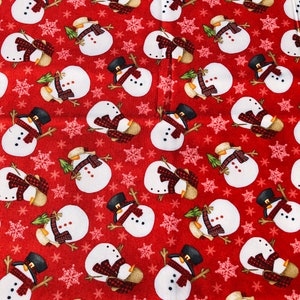 May include: Red fabric featuring a repeating pattern of snowmen and snowflakes. The snowmen have black top hats, red and black plaid scarves, and twig arms. The snowflakes are pink and white.
