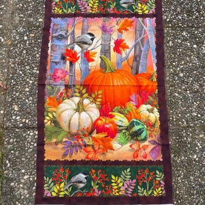 Puede incluir: Panel de tela con una escena de cosecha de otoño. El diseño incluye calabazas, calabacines, hojas coloridas y pájaros. El borde es marrón oscuro con un patrón floral verde y rojo. El fondo muestra abedules.