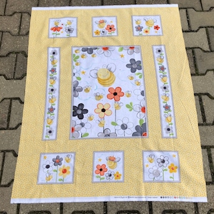 Op de afbeelding: Een geel stoffen paneel met een herhalend patroon van kleine gele stippen. Het paneel heeft een centraal ontwerp van bloemen en bijen, met kleinere vierkante panelen van bijen en bloemen. Het ontwerp bevat oranje, grijze en witte bloemen.