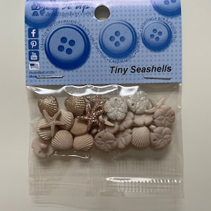 Könnte beinhalten: Eine Tüte mit kleinen Muschelknöpfen in Weiß, Rosa und Gold. Die Tüte ist mit "Tiny Seashells" beschriftet und für Basteln, Kartenherstellung, Quilten, Nähen und Scrapbooking geeignet.