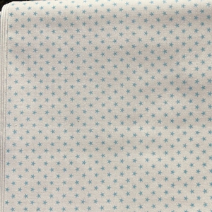 May include: Off-white fabric with a repeating pattern of small, light blue star shapes. The fabric has a textured appearance, and the stars are evenly spaced across the surface. The edge of the fabric is visible on the left side.