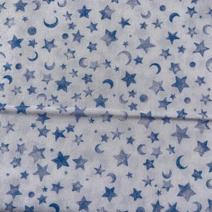 Könnte beinhalten: Weißer Stoff mit einem sich wiederholenden Muster aus blauen Sternen, Monden und kleinen Punkten. Das Himmelsdesign ist gleichmäßig verteilt und erzeugt eine skurrile und verträumte Ästhetik.