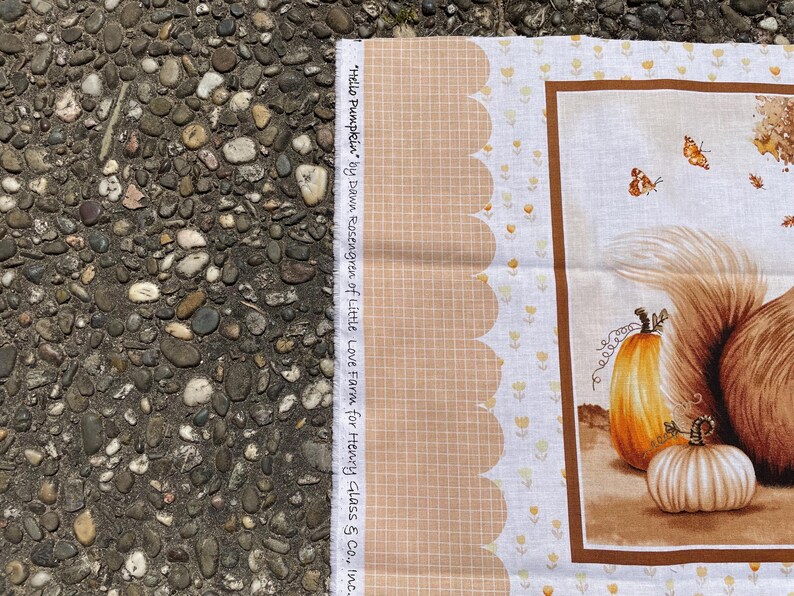 K&ouml;nnte beinhalten: Stoffpaneel mit einer herbstlichen Illustration mit K&uuml;rbissen und Schmetterlingen. Das Design hat einen braunen Rand und einen gewellten Rand mit floralen Akzenten. Der Text lautet "Hello Pumpkin" von Dawn Rosengren of Little Love Farm for Henry Glass & Co., Inc.
