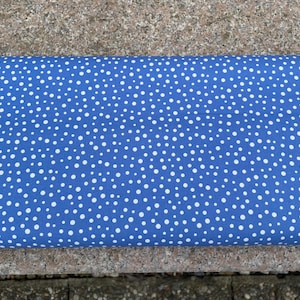 May include: Rolled blue fabric with a white polka dot pattern. The fabric is a vibrant blue color with small, evenly spaced white dots. The fabric is folded over, showing the pattern and texture.