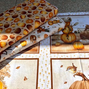 K&ouml;nnte beinhalten: Stoffrollen mit herbstlichen Mustern. Eine Rolle zeigt K&uuml;rbisse in Orange- und Braunt&ouml;nen auf beigem Hintergrund. Eine andere zeigt eine Herbstszene mit K&uuml;rbissen, einer Vogelscheuche und einem Bauernhaus. Der dritte Stoff hat ein K&uuml;rbis- und Vogeldesign.