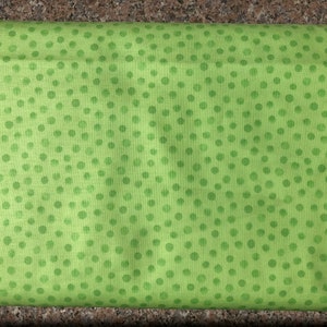 Puede incluir: Un rollo de tela verde claro con un patrón repetitivo de lunares verdes oscuros. La tela tiene un aspecto suave y ligeramente texturizado, adecuado para diversos proyectos de costura y artesanía.