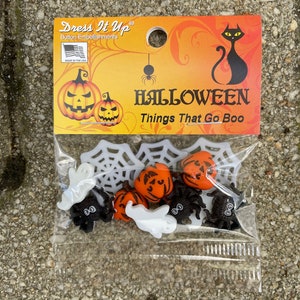 Könnte beinhalten: Eine Packung Halloween-Knöpfe mit Motiven von einer schwarzen Katze, einer Spinne, einem Geist und einem Kürbis. Die Verpackung lautet "Dress It Up Button Embellishments" und "Halloween Things That Go Boo".