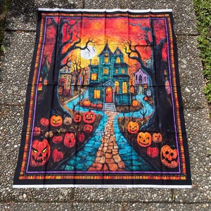 May include: A rectangular fabric panel featuring a Halloween scene with a haunted house, a stone path, and numerous jack-o'-lanterns under a moonlit orange and purple sky. The border is black with orange and purple stripes. Text at the bottom reads: "© Morris Creative Group 2021 for QT Fabrics www.QTFabrics.com 25364-X".