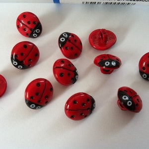 Könnte beinhalten: Zehn rote Marienkäfer-Knöpfe mit schwarzen Punkten und weißen Augen. Die Knöpfe haben eine flache Rückseite mit einem kleinen Loch zum Nähen.