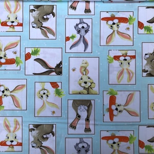 May include: A light blue fabric with a repeating pattern of bunnies holding carrots. The bunnies are in white frames on a light blue background with white polka dots.