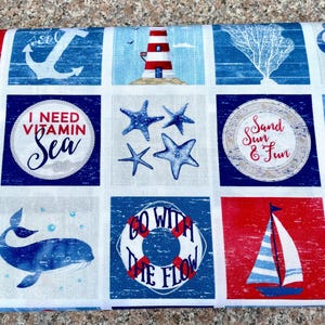 Könnte beinhalten: Stoff mit nautischem Thema mit Quadraten mit Ankern, Leuchttürmen, Segelbooten, Walen und Seesternen. Der Text enthält "I Need Vitamin Sea", "Sand Sun & Fun" und "Go With The Flow". Das Farbschema ist rot, weiß und blau.