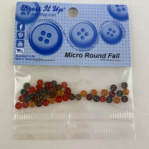 Könnte beinhalten: Eine transparente Tüte mit kleinen, runden Knöpfen in Herbstfarben. Das blaue Etikett trägt die Aufschrift "Dress It Up" und "Micro Round Fall". Die Knöpfe sind in Rot-, Braun-, Orange- und Grüntönen gehalten.