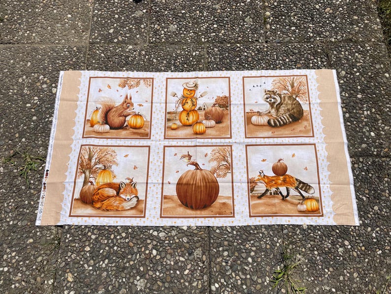 K&ouml;nnte beinhalten: Stoffpaneel mit sechs Quadraten mit herbstlichen Illustrationen. Jedes Quadrat zeigt K&uuml;rbisse und Waldtiere wie Eichh&ouml;rnchen, Waschb&auml;ren und F&uuml;chse. Die Farbpalette umfasst warme Braun- und Oranget&ouml;ne, die die Jahreszeit widerspiegeln.