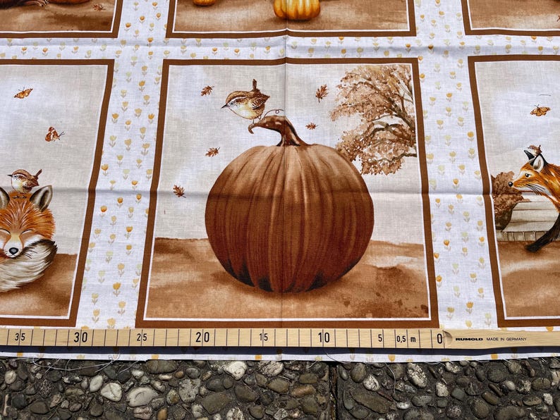 K&ouml;nnte beinhalten: Stoff mit sich wiederholendem Muster mit braunen K&uuml;rbissen, F&uuml;chsen und V&ouml;geln. Das Design umfasst einen gro&szlig;en K&uuml;rbis mit einem Vogel, der darauf sitzt, umgeben von fallenden Bl&auml;ttern. Der Hintergrund ist hellbeige mit kleinen gelben floralen Akzenten.