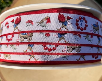 Könnte beinhalten: Eine Spule mit weißem Band mit einem sich wiederholenden Muster aus Rotkehlchen, Pilzen und Figuren in blauen und roten Outfits. Das Band hat einen roten Rand und wird auf einer weißen Spule präsentiert.