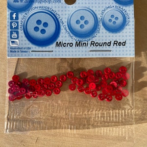 Könnte beinhalten: Eine transparente Tüte mit kleinen, roten, runden Knöpfen. Die Verpackung trägt den Text "Micro Mini Round Red" und die Marke "Dress It Up". Die Knöpfe eignen sich für Basteln, Nähen und Scrapbooking.
