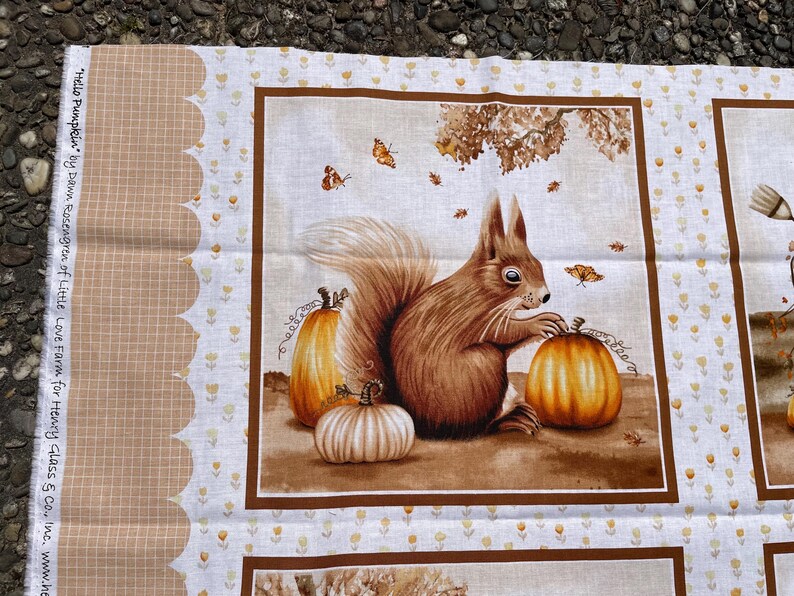 K&ouml;nnte beinhalten: Stoffpaneel mit einem braunen Eichh&ouml;rnchen und K&uuml;rbissen, Schmetterlingen und Bl&auml;ttern. Die Illustration enth&auml;lt den Text "Hello Pumpkin" und den Namen des K&uuml;nstlers. Herbstliches Thema.